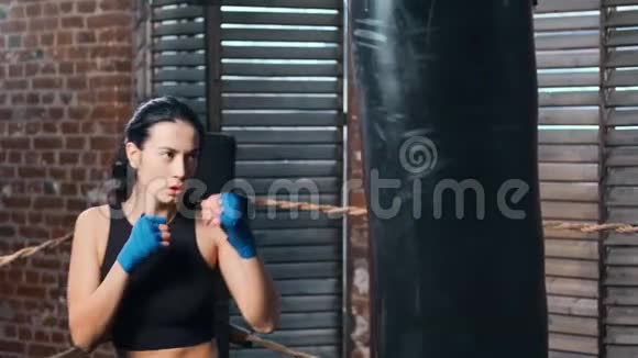强悍的黑发女子mma拳手在健身房慢动作训练中的拳打脚踢袋视频的预览图