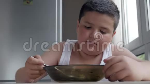 可爱的小胖男孩在厨房里吃饭吃一大勺汤儿童肥胖和暴食的概念视频的预览图