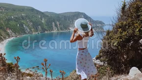 美丽的金发女人在海风中戴着太阳帽欣赏希腊凯法洛尼亚岛的海岸线景色幸福快乐视频的预览图