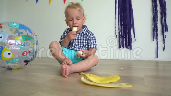 可爱的婴儿坐在地板上吃香蕉手拿香蕉的帅哥视频的预览图