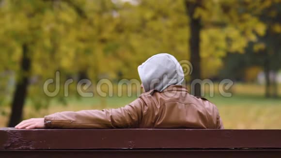 一个不知名的危险人物坐在一个秋天的公园里坐在长凳上看着copspace视频的预览图