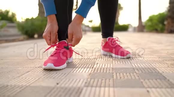 女人在运动鞋上系鞋带把耳机插入耳朵日落时开始沿着棕榈街奔跑视频的预览图