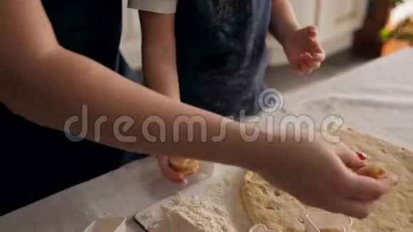 母亲和女儿穿着围裙切出不同形状的饼干面团视频的预览图