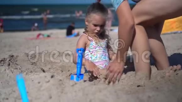 迷人的女人在沙滩上挖小女孩妈妈和女儿玩得开心视频的预览图