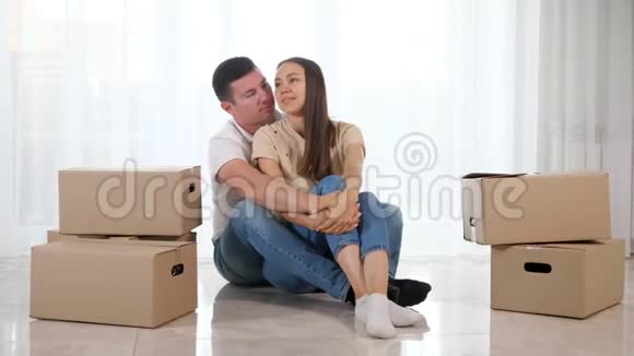 穿牛仔裤的男人女人坐在新房子的光地板上拥抱视频的预览图