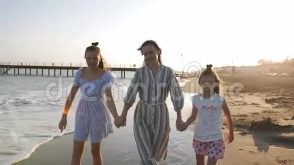 幸福的母亲与两个女儿7年和13年的步行在沙岸日落视频的预览图