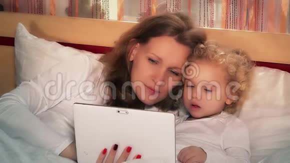 年轻的女人和可爱的小女孩用平板电脑坐在床上视频的预览图