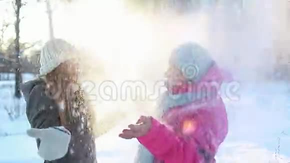 冬季趣味活动母亲和成年女儿在户外用雪摇动冷杉树枝一家人笑视频的预览图
