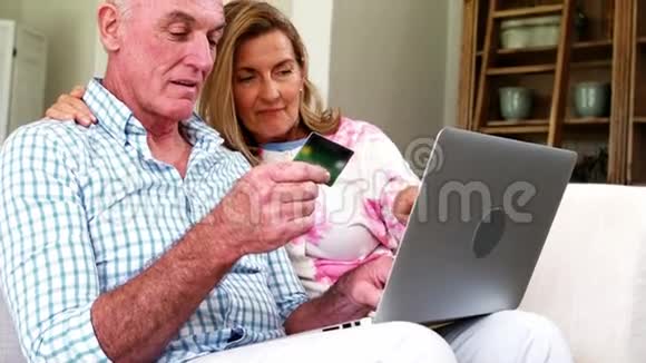 在客厅里用笔记本电脑在网上购物时微笑的老夫妇视频的预览图