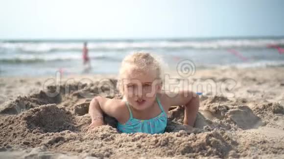 五岁的女孩被埋在沙子里挣脱逃跑了模糊的人和海洋视频的预览图