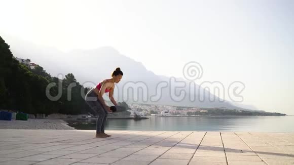 穿运动服装的运动女子在海上码头展开瑜伽垫视频的预览图
