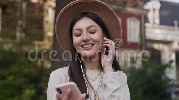 她微笑着戴着可爱的帽子站在豪宅院子里用耳机听音乐视频的预览图
