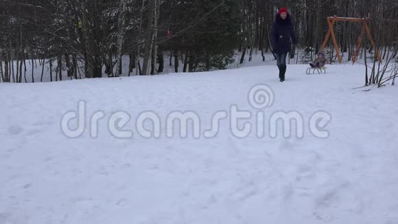 女家长拉雪橇与婴儿在公园覆盖雪4K视频的预览图