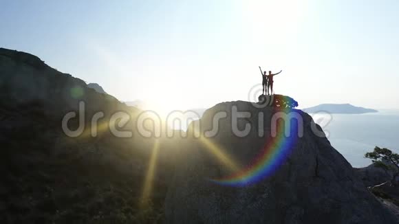 日出时一对相爱的夫妇站在山顶上挥舞着双手飞行航班视频的预览图