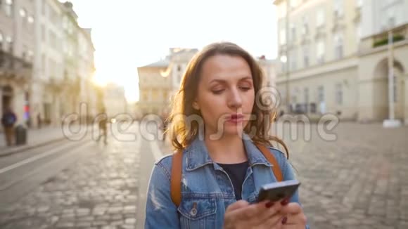 女人走在一条老街上用智能手机她很高兴看到那里赢或大运概念慢慢视频的预览图