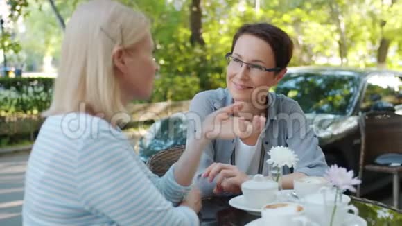 有魅力的成年女性在户外咖啡馆里用饮料在餐桌上打手势视频的预览图
