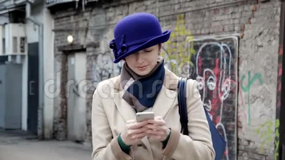戴着蓝帽子的漂亮女孩近距离在4K街上微笑着看留言电话视频的预览图