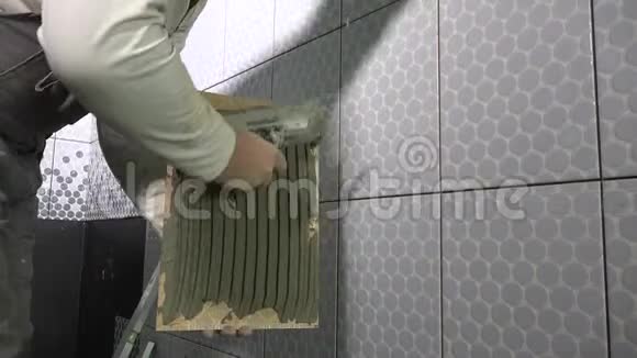 熟练的人在瓷砖上涂胶水然后把它安装到墙上穿脏衣服的工人视频的预览图