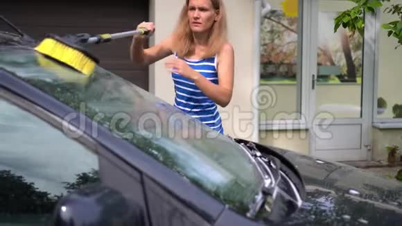 妻子刷丈夫的汽车挡风玻璃与长刷洗发水泡沫视频的预览图