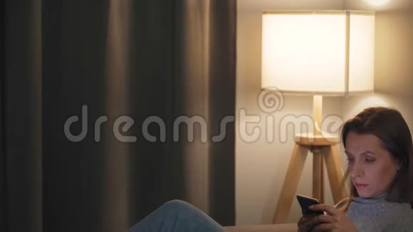 女人躺在舒适的房间里晚上用智能手机上网网上购物视频的预览图