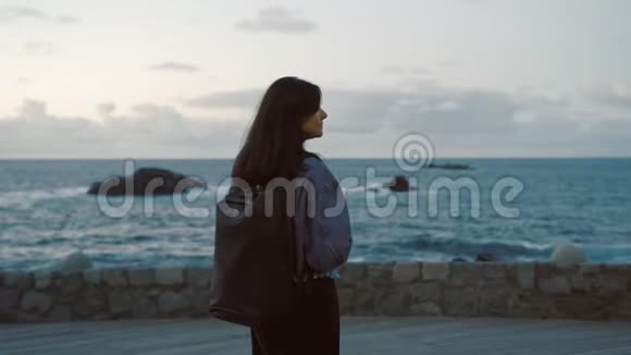 一位年轻的女游客晚上背着背包在海边散步视频的预览图