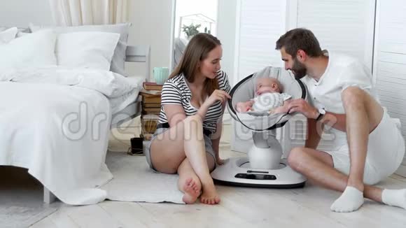 一群幸福的父母看着他们的小宝宝在一间白色公寓里的家里坐着摇椅睡觉这就是视频的预览图