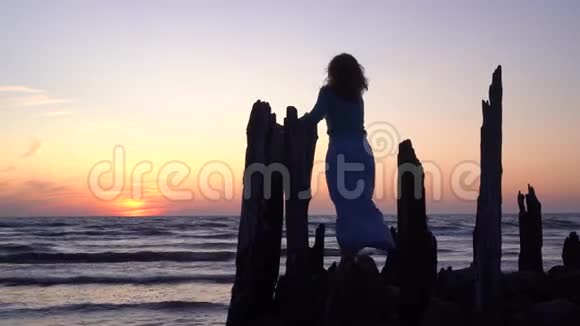 浪漫的女人在橙色的夕阳下在古老的海上码头石头和树林中摆姿势视频的预览图