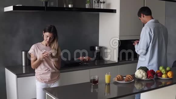 年轻夫妇在厨房的智能手机屏幕上看着一些现代阁楼设计的东西晨读视频的预览图
