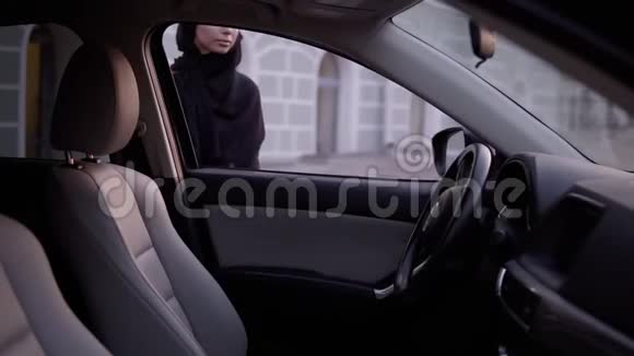 年轻漂亮的穆斯林女孩戴着黑色头巾打开门坐在车里看着镜子修理它插入视频的预览图