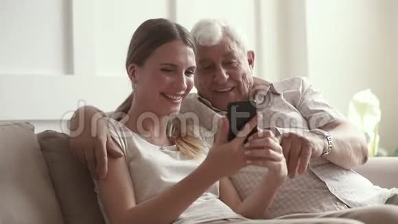 幸福的家庭高级退休父亲拥抱成年女儿智能手机视频的预览图