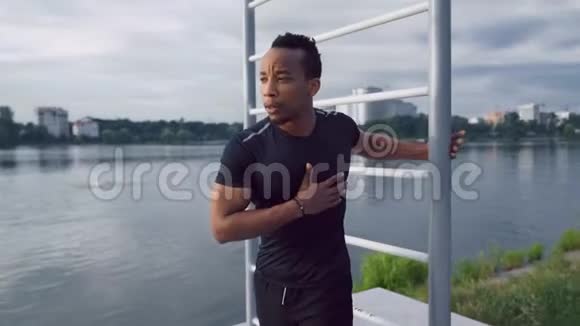 美国黑人健身男子在户外靠近墙杆伸展身体视频的预览图