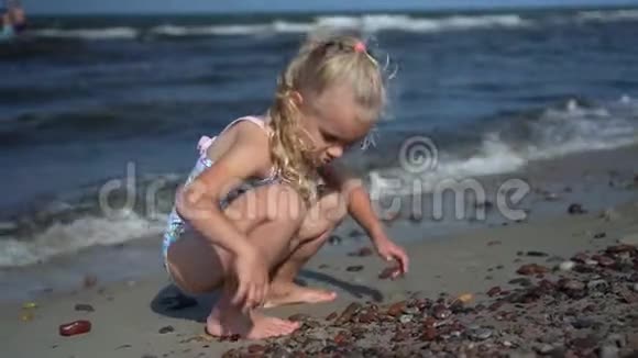 美丽的金发女孩在海边玩石子海浪视频的预览图
