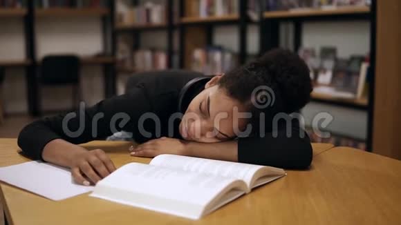 一个穿黑色毛衣的美国黑人女学生累了在一张桌子上睡着了桌子上有现代的书籍和笔记视频的预览图