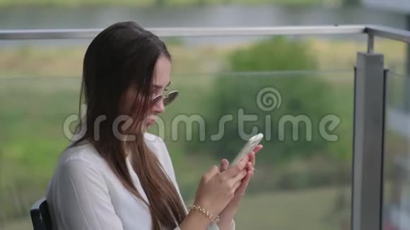 夏天坐在露台上的年轻女子在智能手机上输入短信视频的预览图