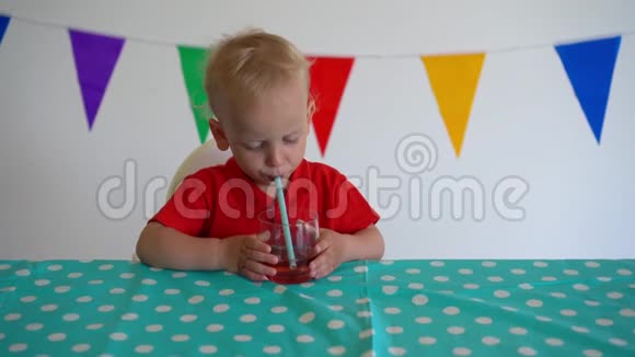 可爱的小男孩坐在桌子旁用吸管喝苹果汁万向节视频的预览图