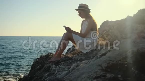 女孩独自享受时光她拿着手机坐在岩石上视频的预览图