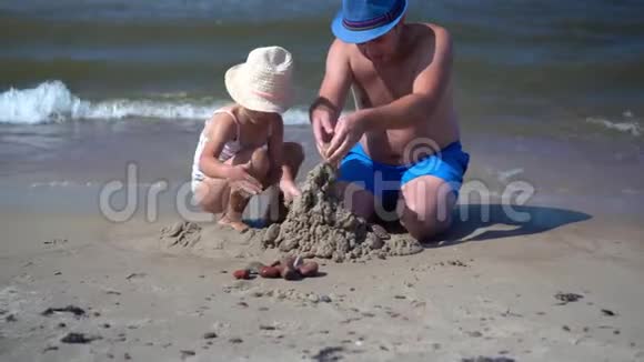 爸爸和小女孩在海上海岸线上建造潮湿的沙堡视频的预览图