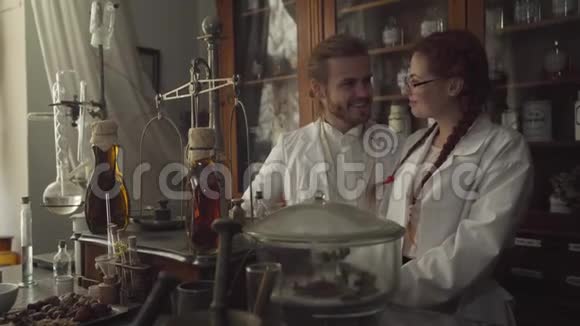 年轻的白种人男人女人看着瓶透明的液体和微笑站在后台的药剂师视频的预览图
