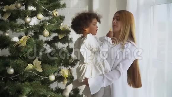 快乐的母亲和穿着白色衣服的小女儿坐在圣诞树旁吃饼干视频的预览图