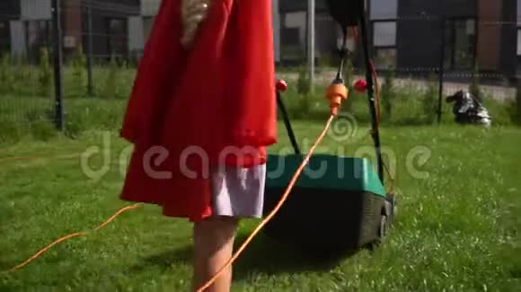 穿红色斗篷的超级女孩子在有栅栏的院子里割草帘线割草机视频的预览图