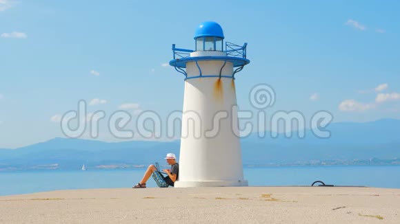 自由职业者在希腊灯塔附近的海边工作很容易找到工作在海边找工作坐着的男人视频的预览图