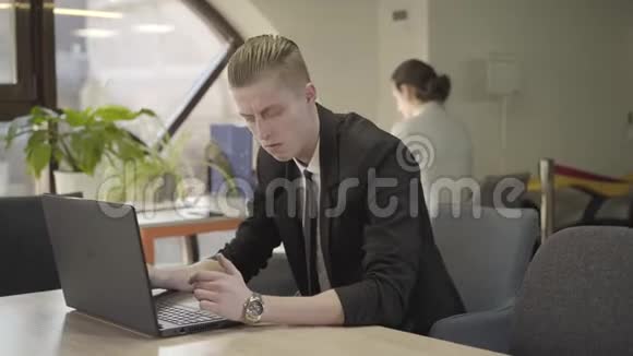 白种人年轻人坐在空地办公室在笔记本电脑键盘上打字的肖像男性办公室职员视频的预览图