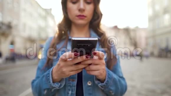 女人在日落时用智能手机沿着一条老街走慢动作背景上的黄色有轨电车视频的预览图