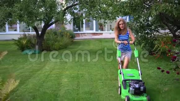 夏季傍晚年轻的金发女子在住宅后花园割草视频的预览图