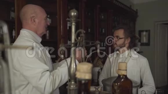 两位兴奋的白人药剂师站在架子的背景上拿着试管说话视频的预览图