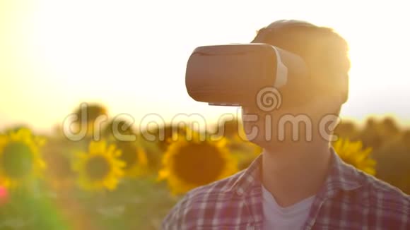 一个年轻人在阳光明媚的日子里用虚拟现实眼镜看着一片向日葵的田野它们是现代科技视频的预览图