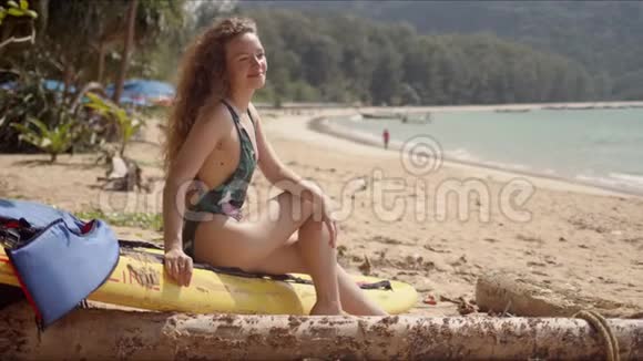 穿着泳装的开朗女人坐在海洋前的黄色游泳板上视频的预览图