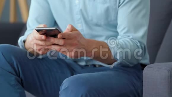 穿着正式的男人坐在沙发上用智能手机发短信特写视频的预览图
