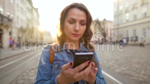 女人走在一条老街上用智能手机她很高兴看到那里赢或好运的概念视频的预览图