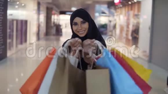 美丽的年轻穆斯林妇女化妆完美购物后拿着各种五颜六色的购物袋微笑着走向视频的预览图